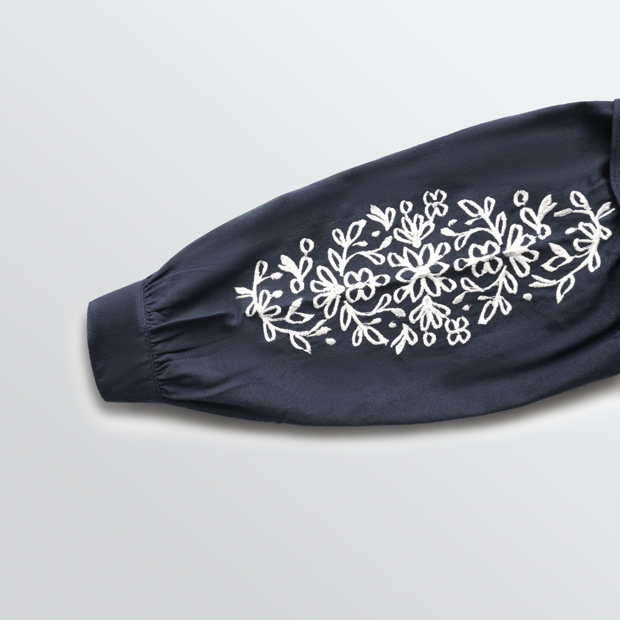 Navy blue sleeve with white floral embroidery on a light gray background